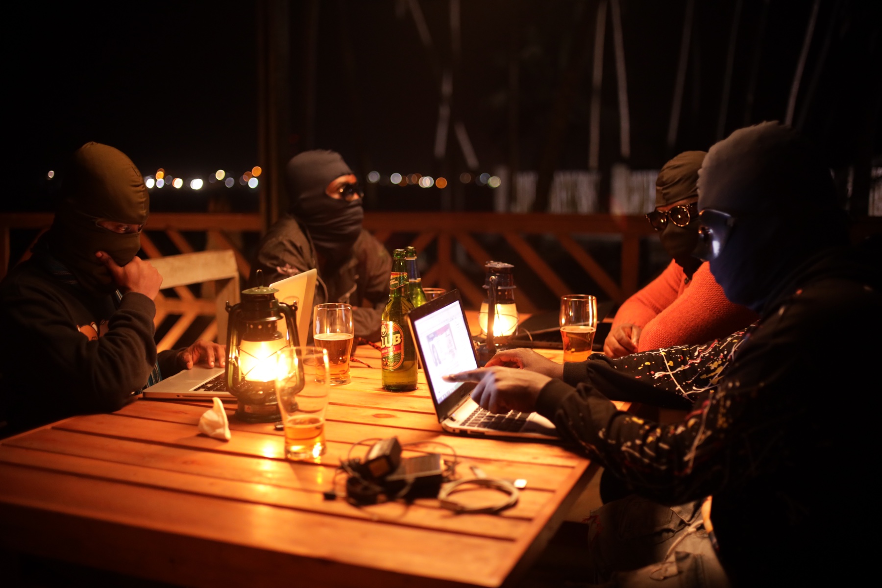 Masked men gathered around laptops at night